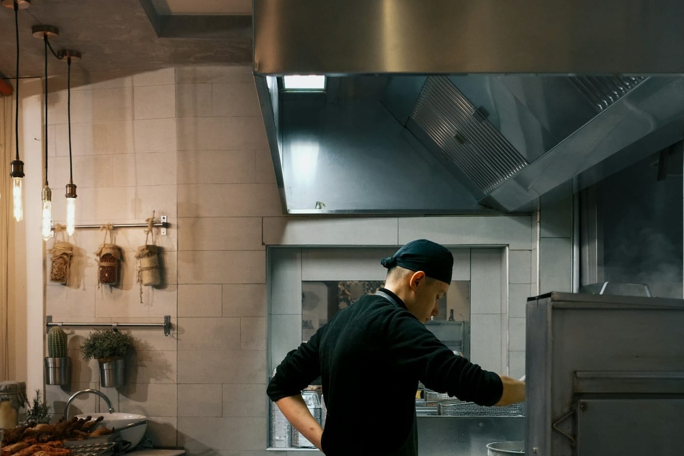 A cook working at a range in a restaurant kitchen, pans and extraction hood above the line.