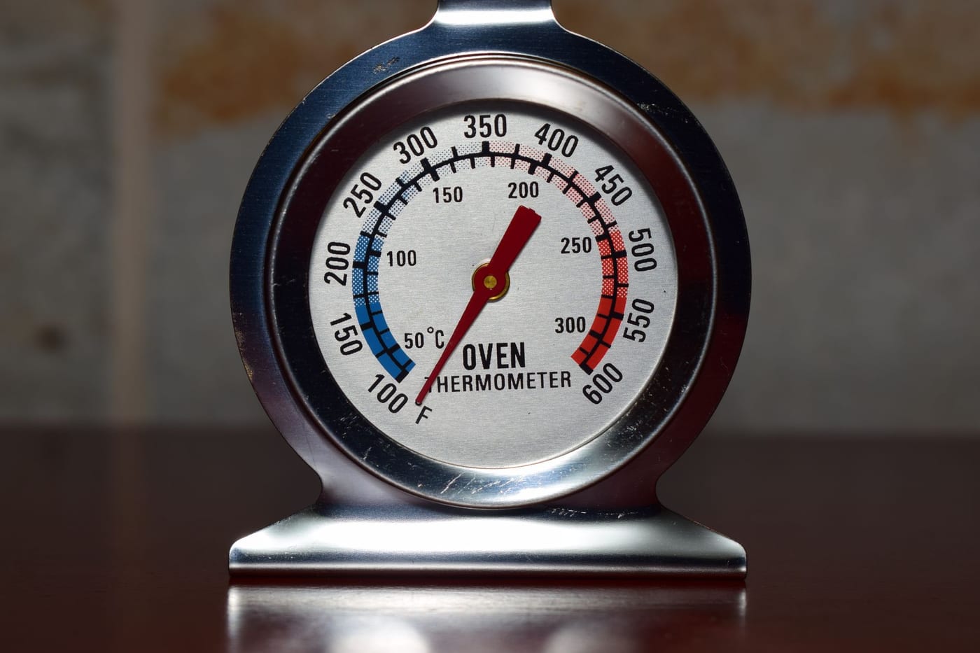 A metal dial oven thermometer standing on a surface, its needle pointing to a marked temperature on a numbered scale.